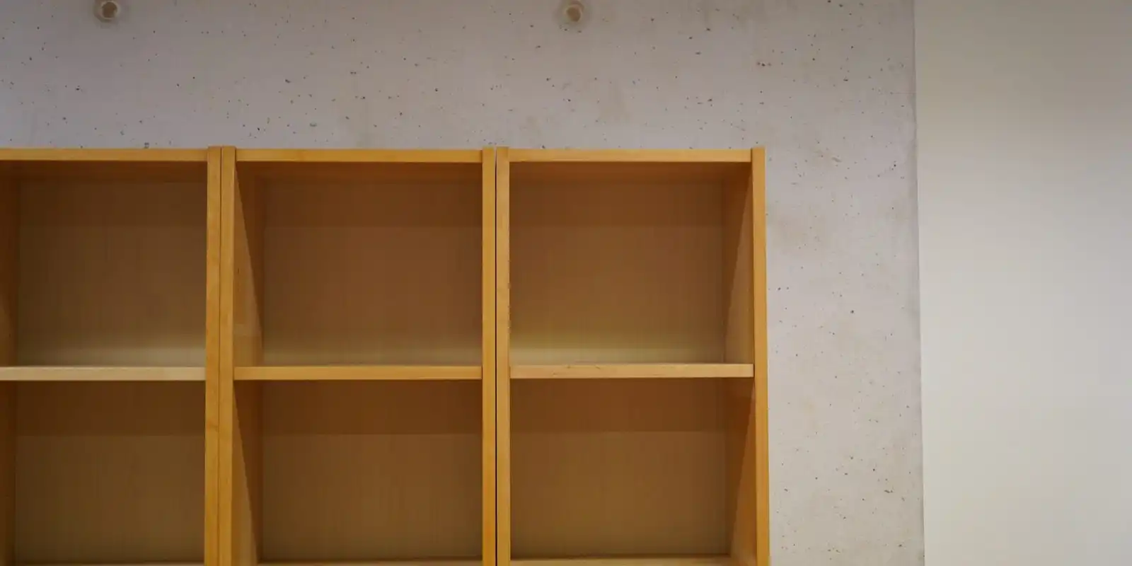 Empty pale wooden shelves against a smooth concrete wall.