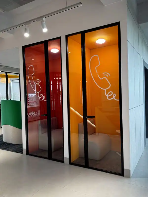 Two glass phone booths in an open office, one lined in red and one in orange, each with a telephone drawn on the glass.