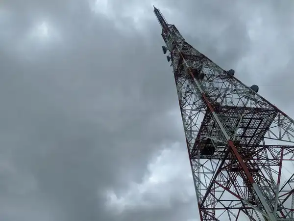 A red and white radio tower seen from its base against a grey, cloudy sky.