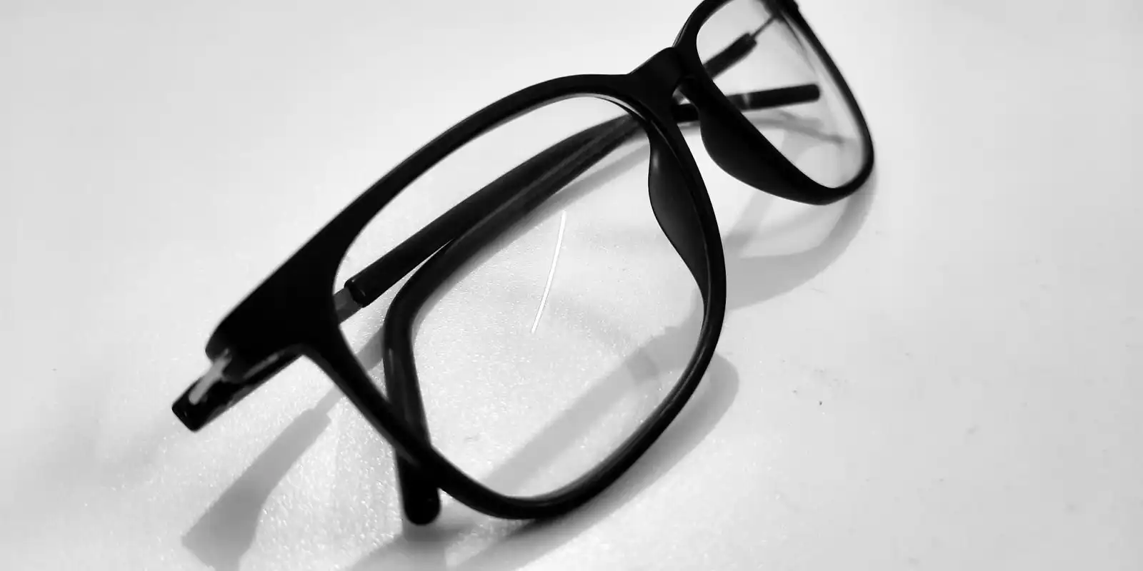 A pair of black-framed reading glasses lying folded on a white table.
