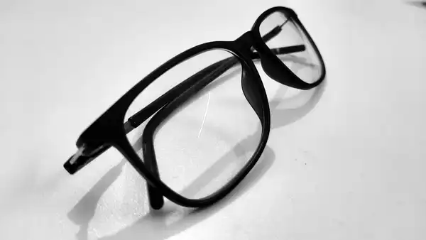 A pair of black-framed reading glasses lying folded on a white table.