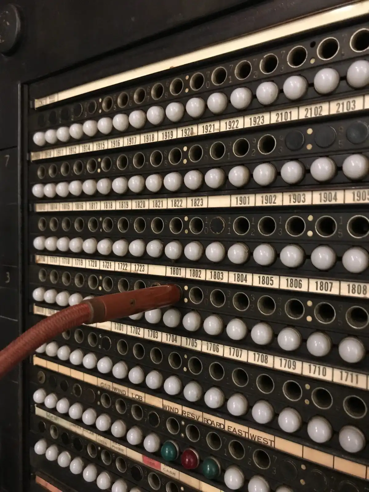 Rows of numbered sockets on an old telephone switchboard, with one thick cord plugged in.