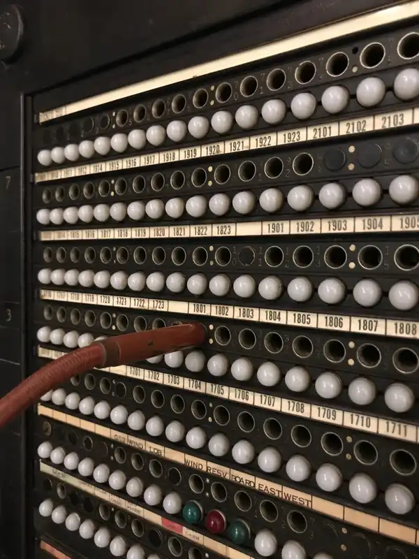 Rows of numbered sockets on an old telephone switchboard, with one thick cord plugged in.